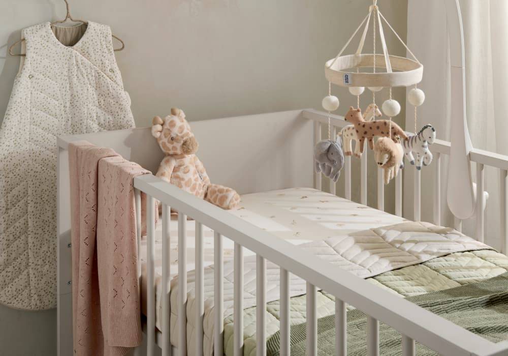 A white crib with bedding and an animal cot mobile.