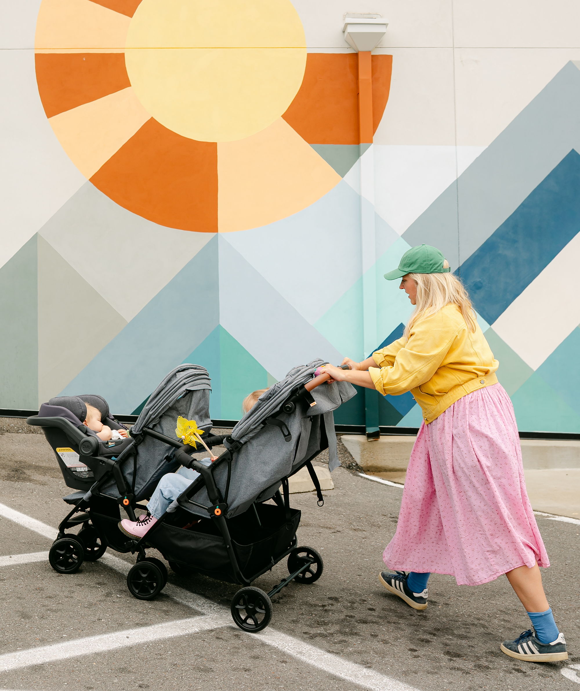 A person pushing a double stroller in front of a colorful mural.