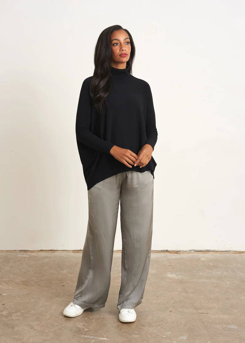 A model wearing a black turtle neck jumoer with light grey satin trousers and white trainers
