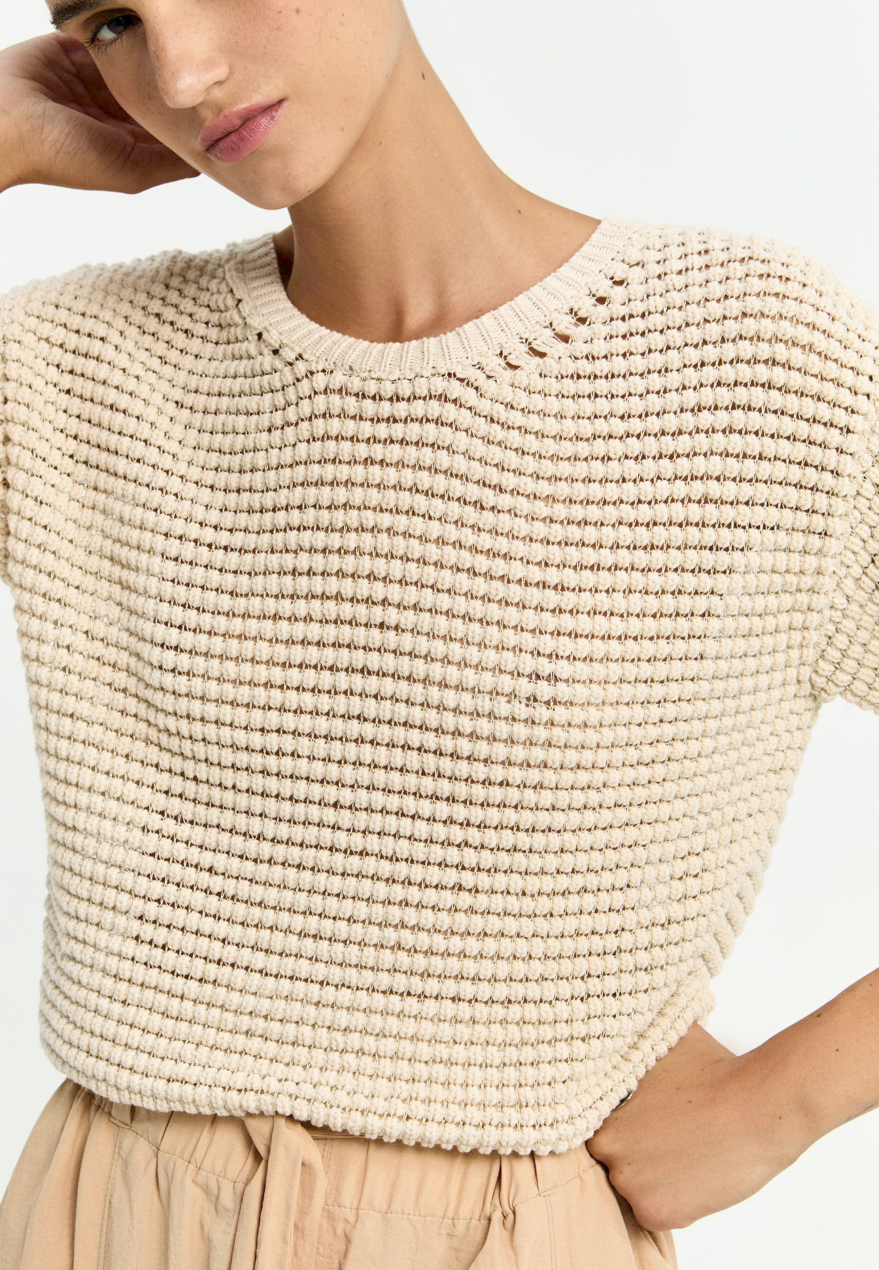 A model wearing a textured, light beige sweater.