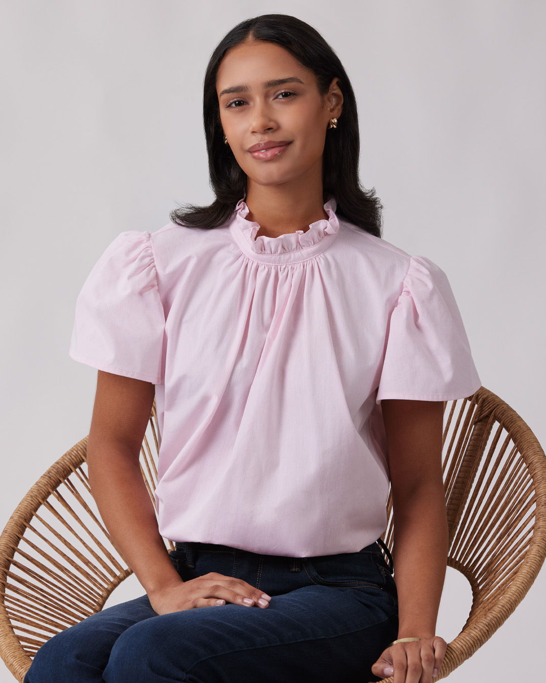 Person wearing a pink blouse, seated in a wicker chair.