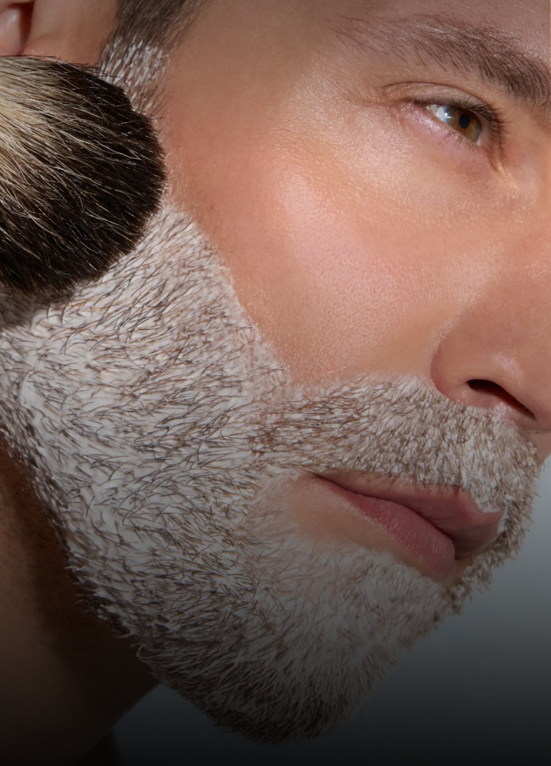 Close-up of a man with a textured beard and makeup brush.