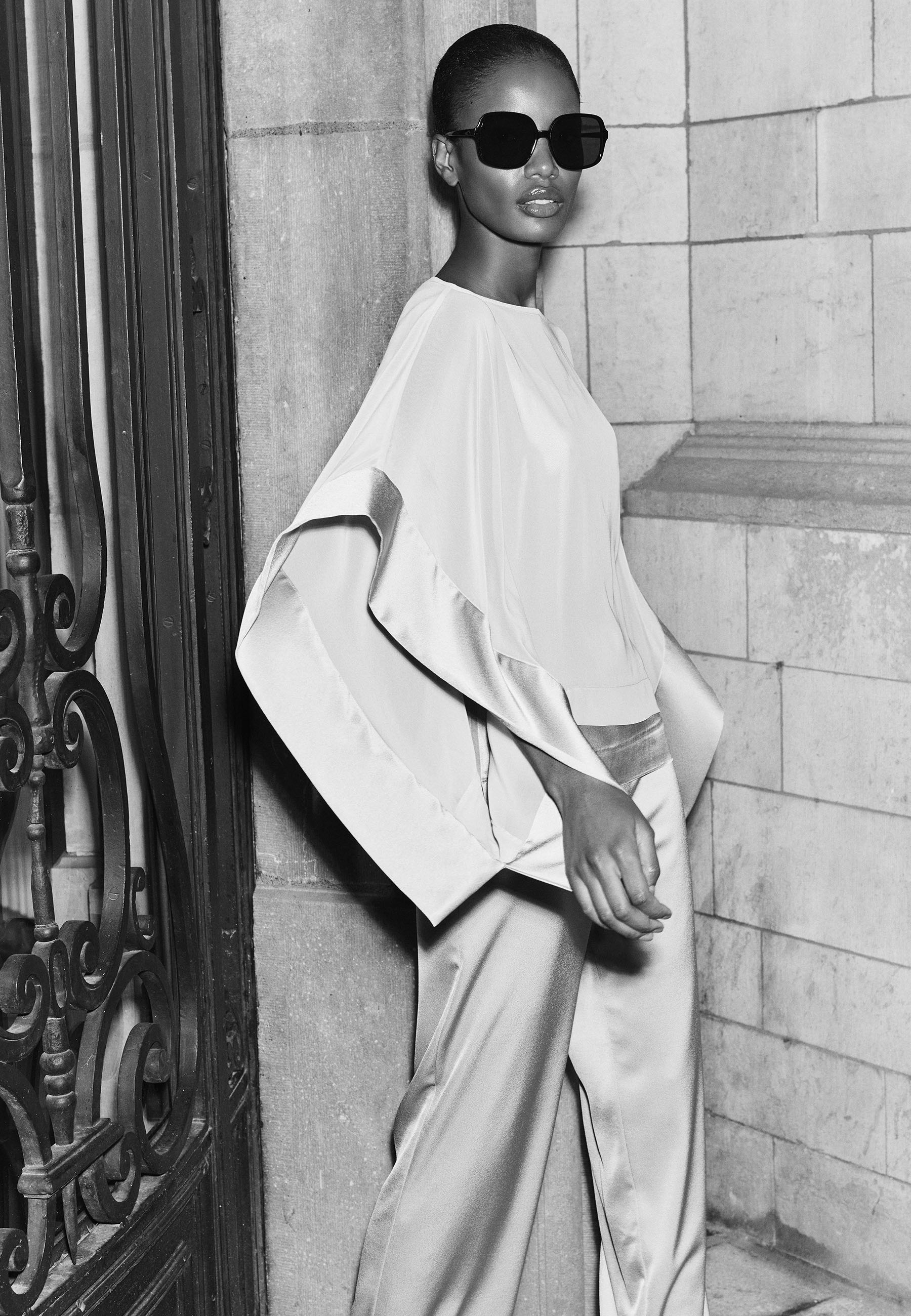 Model wearing stylish outfit and sunglasses near ornate doorway.