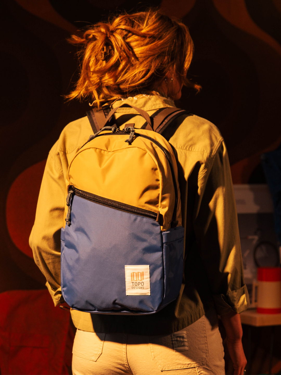 Woman wearing a backpack, viewed from the back, with a colorful background.