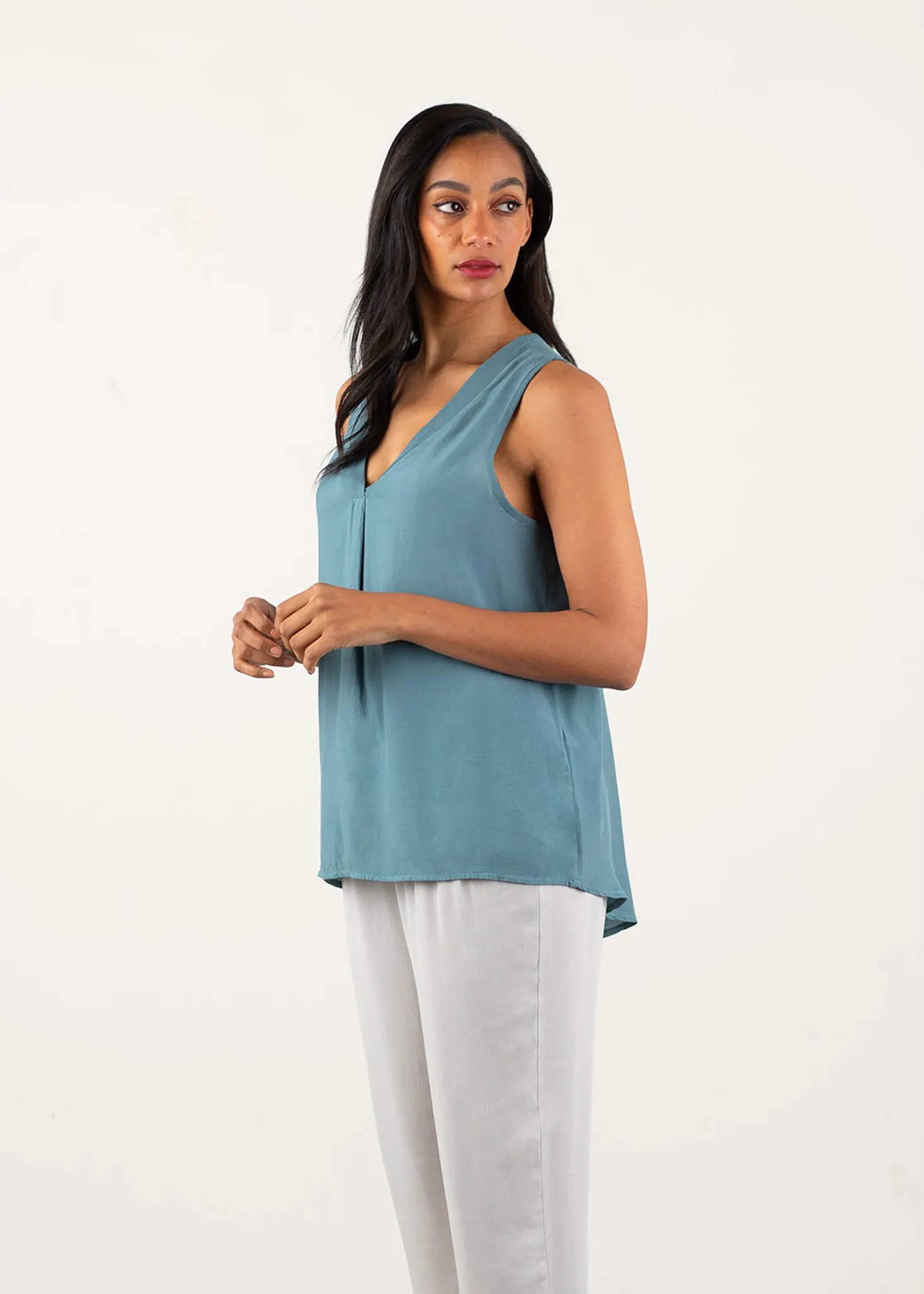 A model wearing a blue grey v neck sleeveless top with  oatmeal coloured trousers