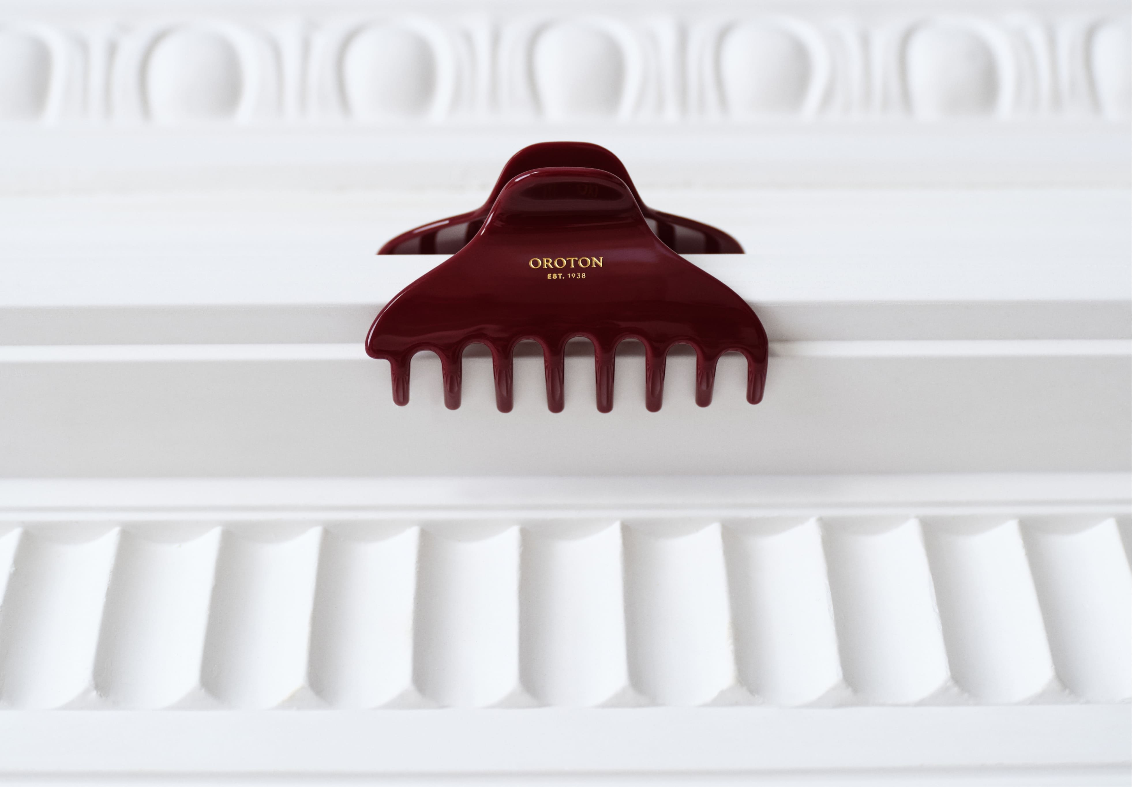 A maroon hair clip resting on a white decorative surface.
