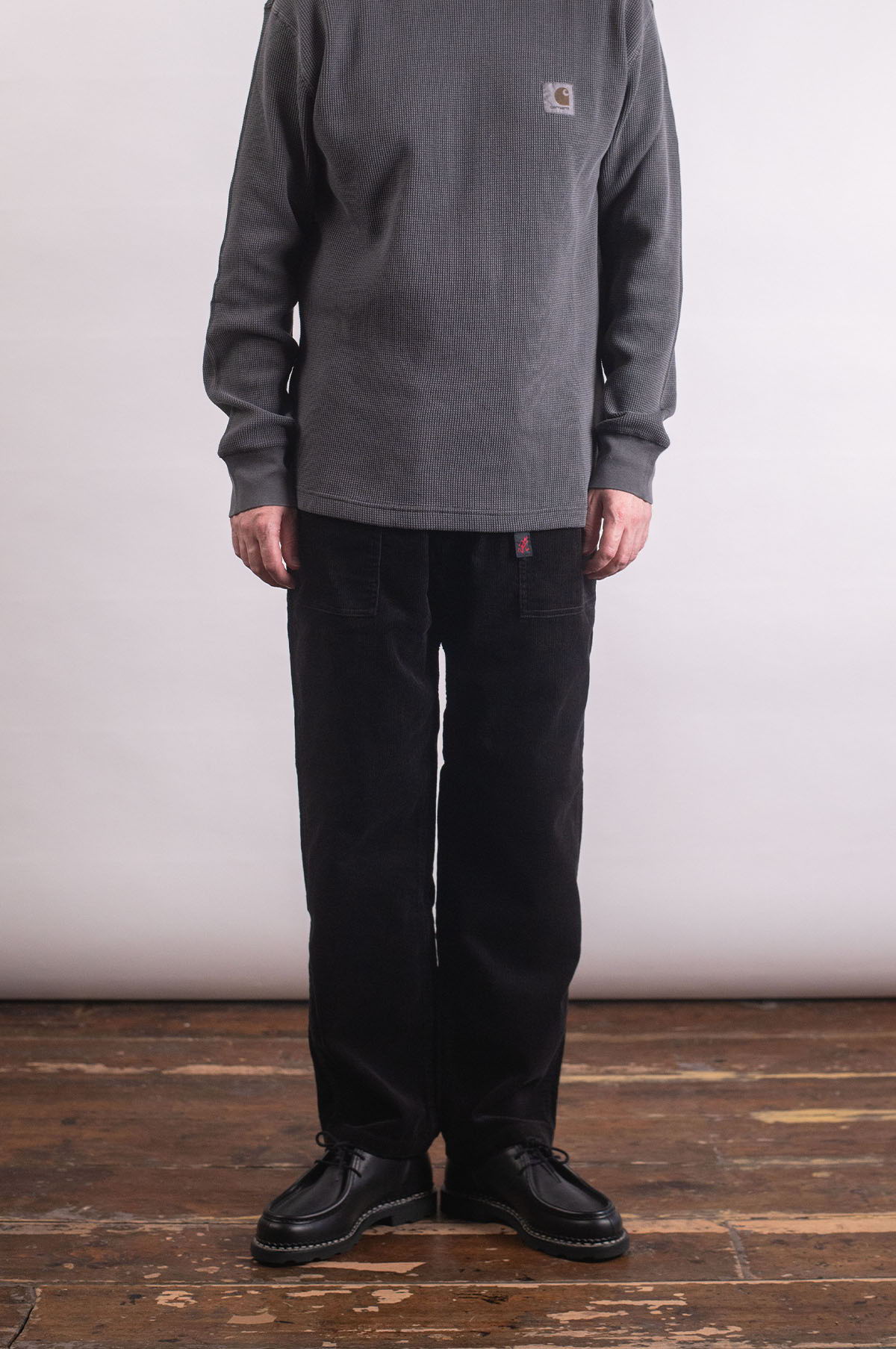 Person wearing a gray sweater and black pants, standing on a wooden floor.