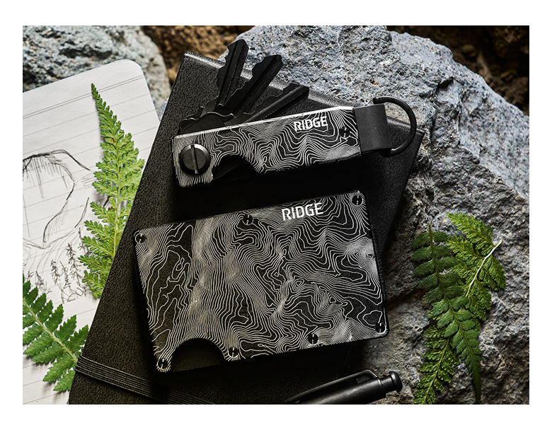 Two sleek wallets on a textured background with foliage and sketchbook.