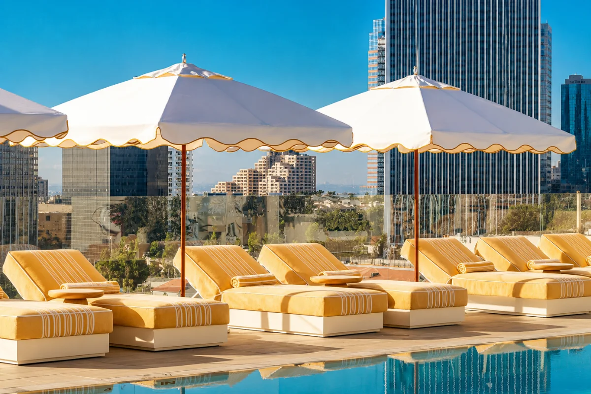 Rooftop hotel pool deck with upholstered chaise lounges and large commercial pool umbrellas overlooking the city