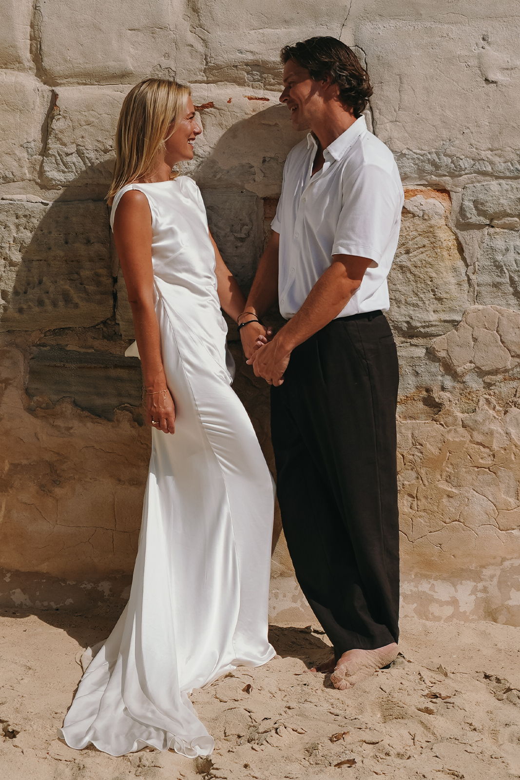 A couple in wedding attire holding hands on the beach.
