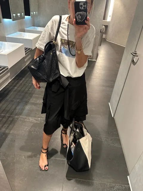 Person in a mirror selfie holding multiple bags, wearing casual black outfit.