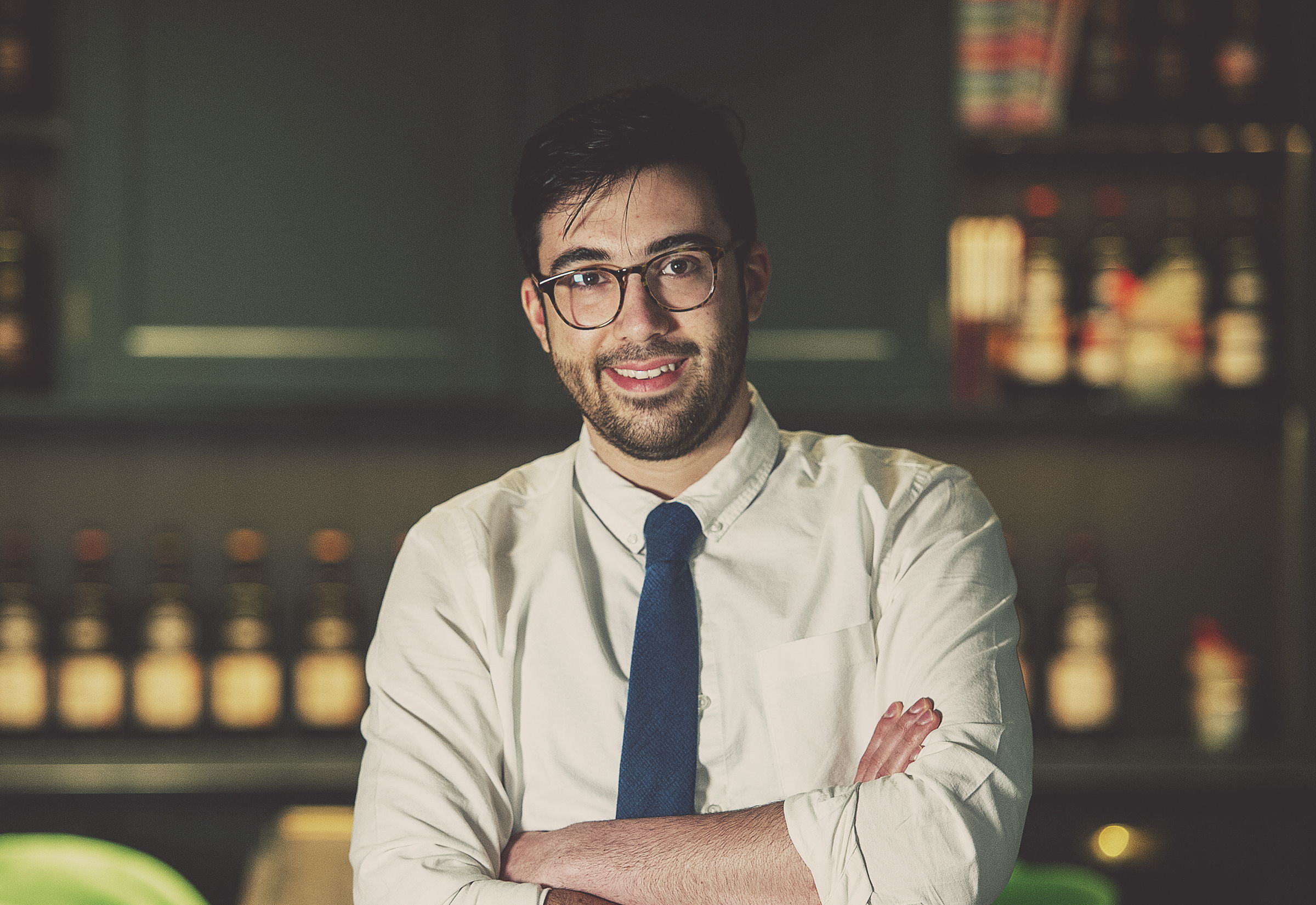 Smiling man in a white shirt and tie stands in a bar setting.