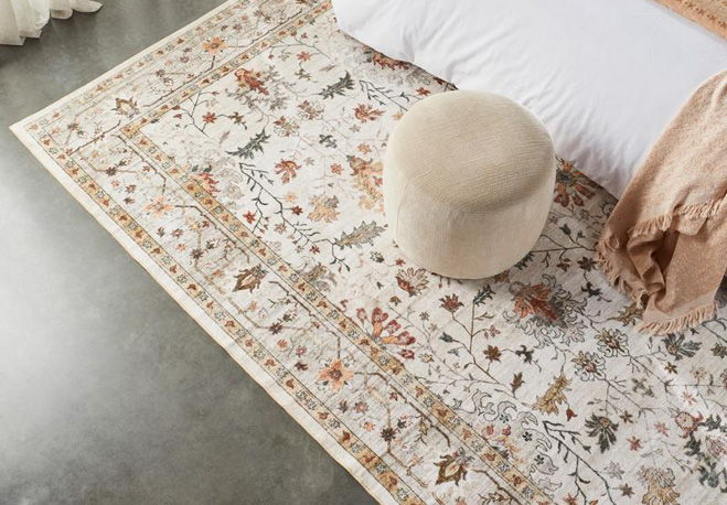 A decorative rug with floral patterns beside a bed and a round stool.
