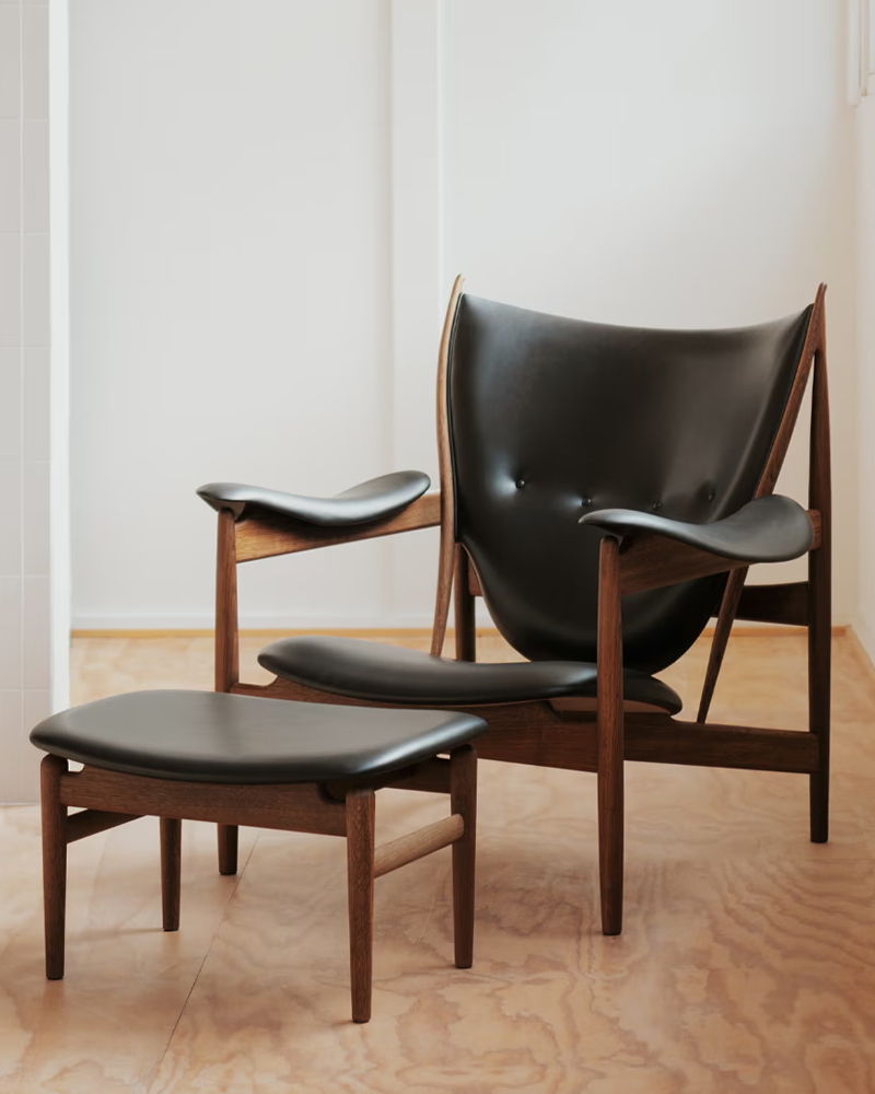 A stylish Chieftain leather chair by House of Finn Juhl with matching ottoman on a wooden floor.