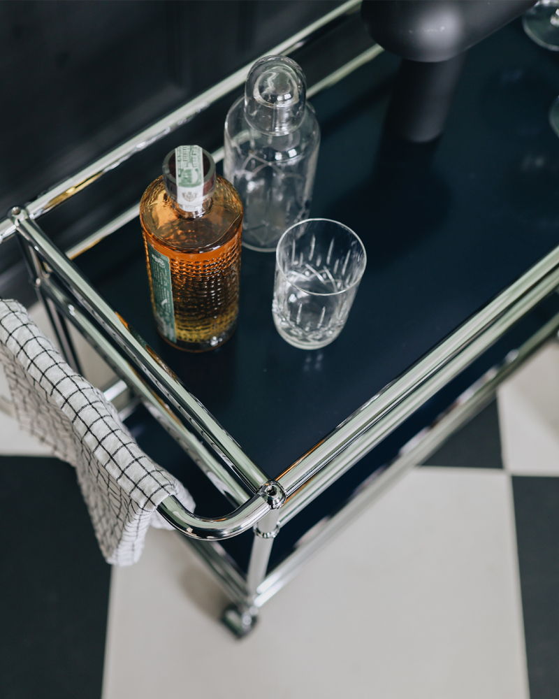 A USM Haller bar cart with a bottle, glasses, and a towel.