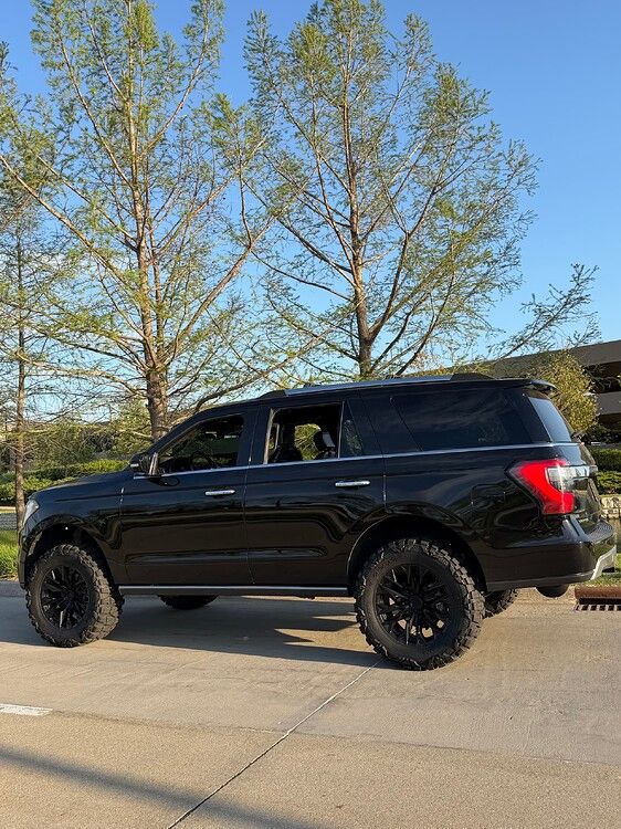 Side profile Troy's black lifted 2018 Ford Expedition with off-road tires and spring trees in background gallery photo 19