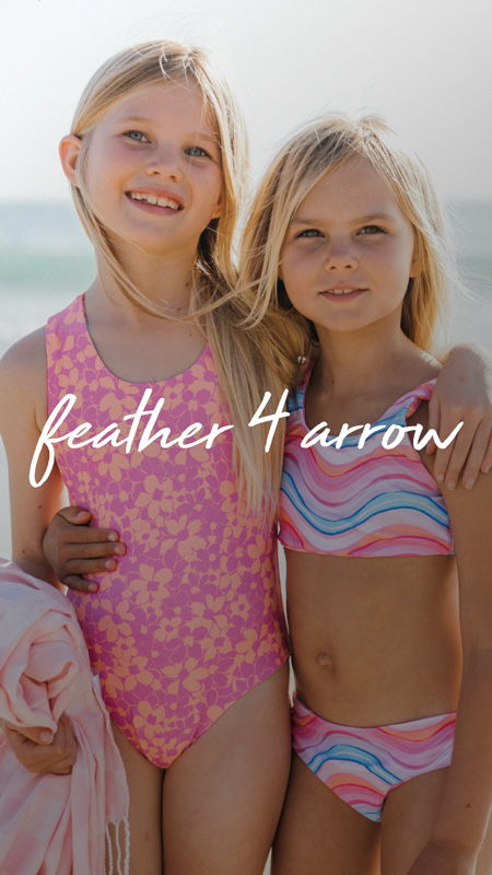 Two girls in swimsuits smiling at the beach.