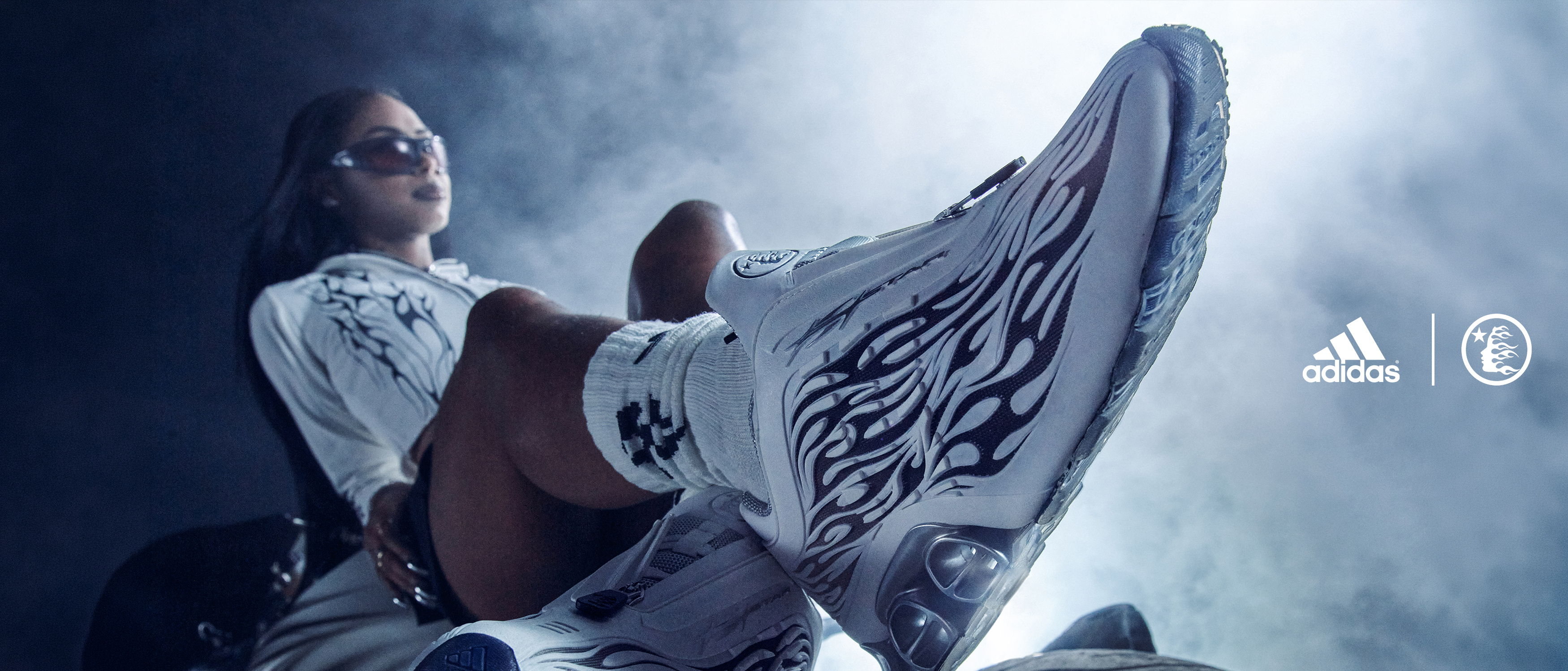 Person wearing stylish footwear, seated with dramatic lighting and logo elements.