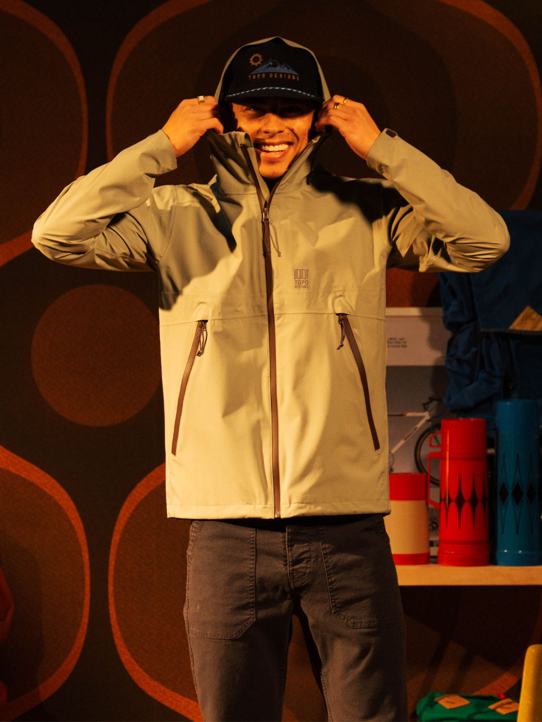 Person wearing a gray jacket and cap, smiling while adjusting the hood.