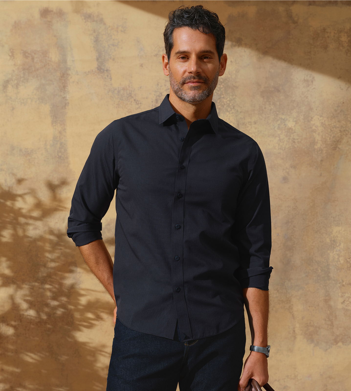 Man in a black shirt stands against a textured background.