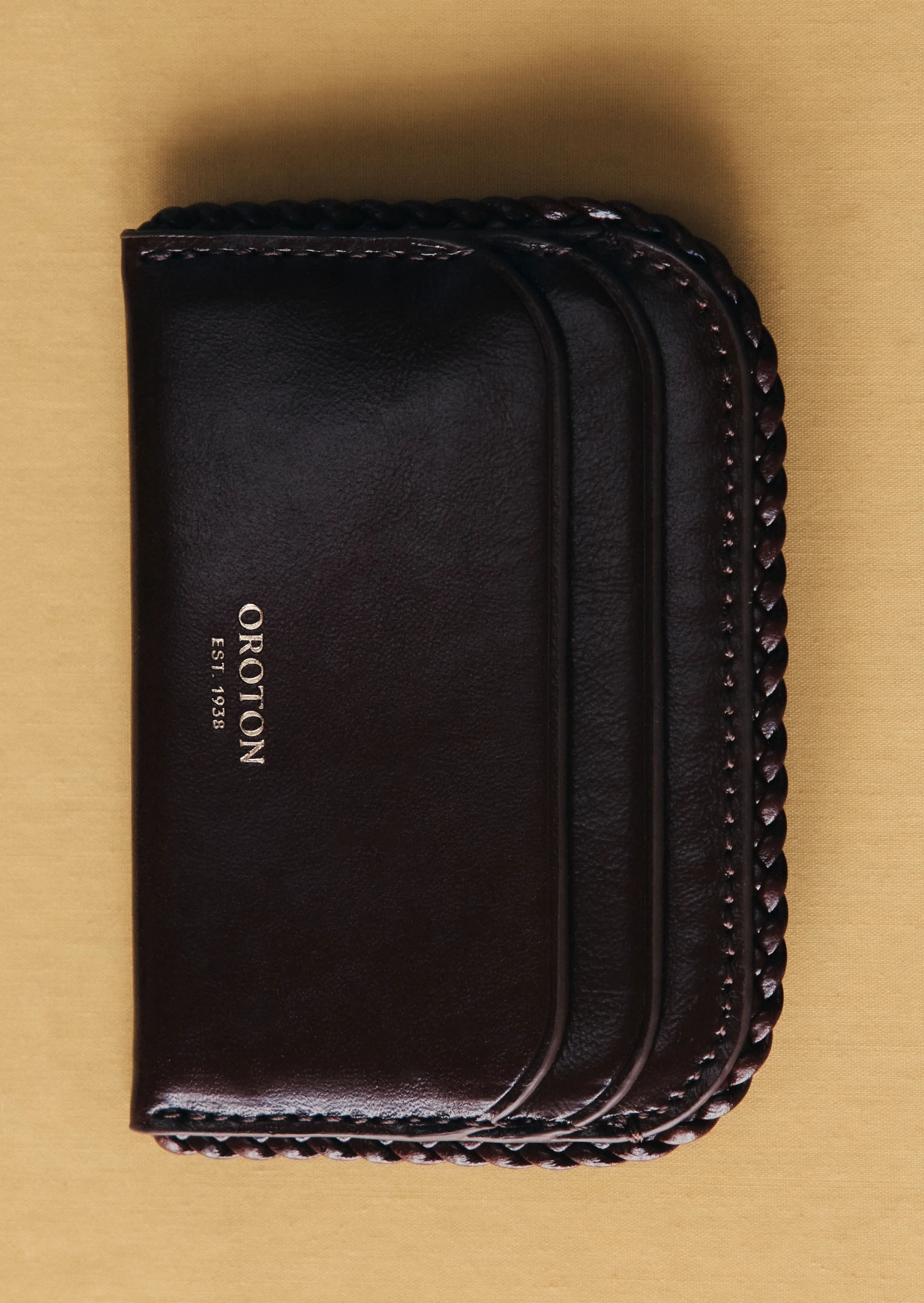 A brown leather wallet with multiple card slots and a braided edge.