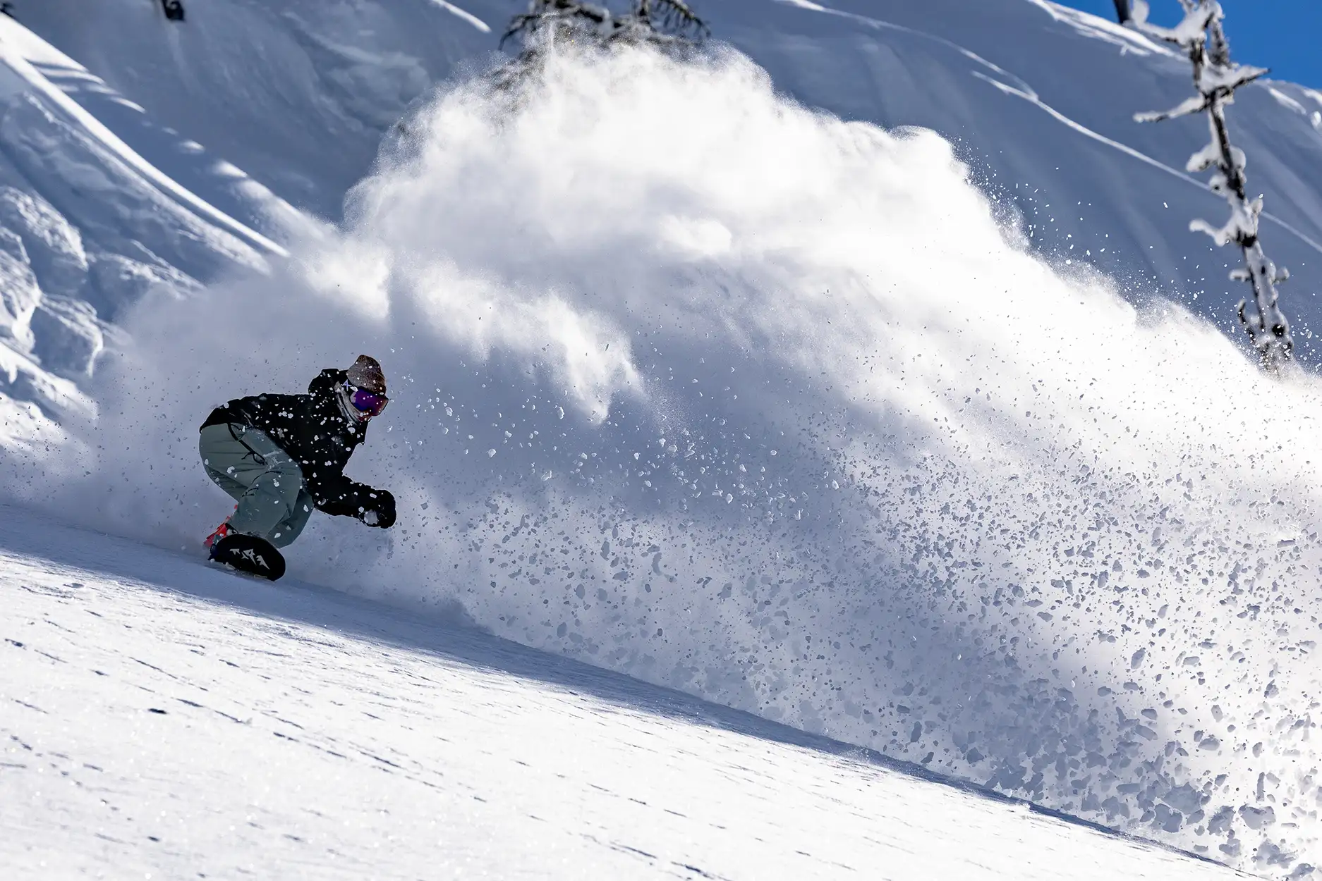 Snowboarder riding down a snowy slope, kicking up powder.