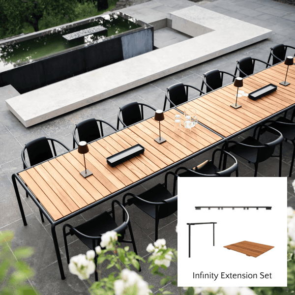Large teak outdoor extension dining table with black chairs and Infinity Extension Set detail on a modern patio.