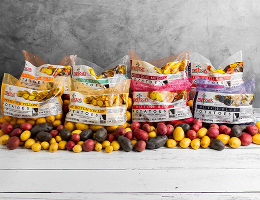 Assorted bags of potatoes on a wooden surface with a gray background.