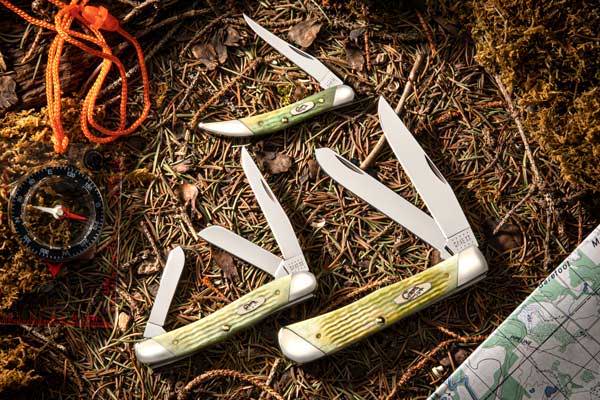 Mint Green Bone Medium Stockman, Small Texas Toothpick and Trapper knives shown on forest floor pine needles with compass and topography map