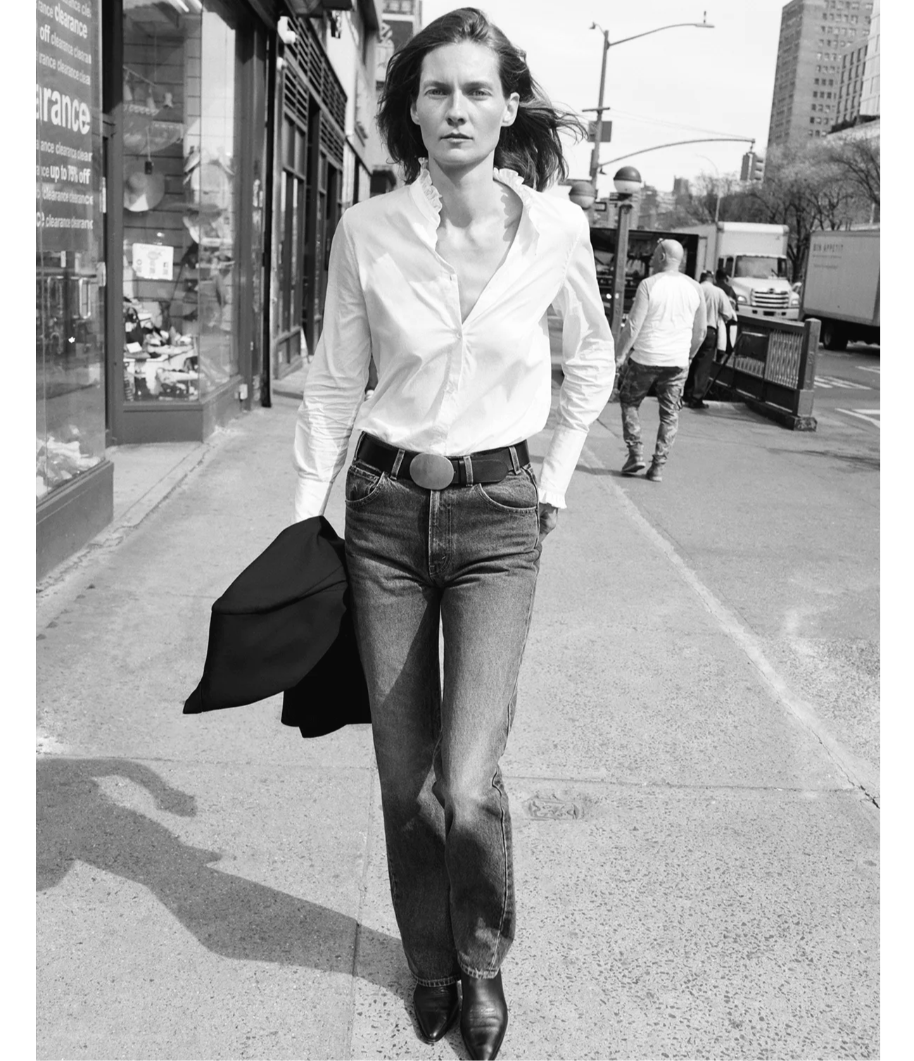 A person walking on the street, wearing a white shirt and jeans.