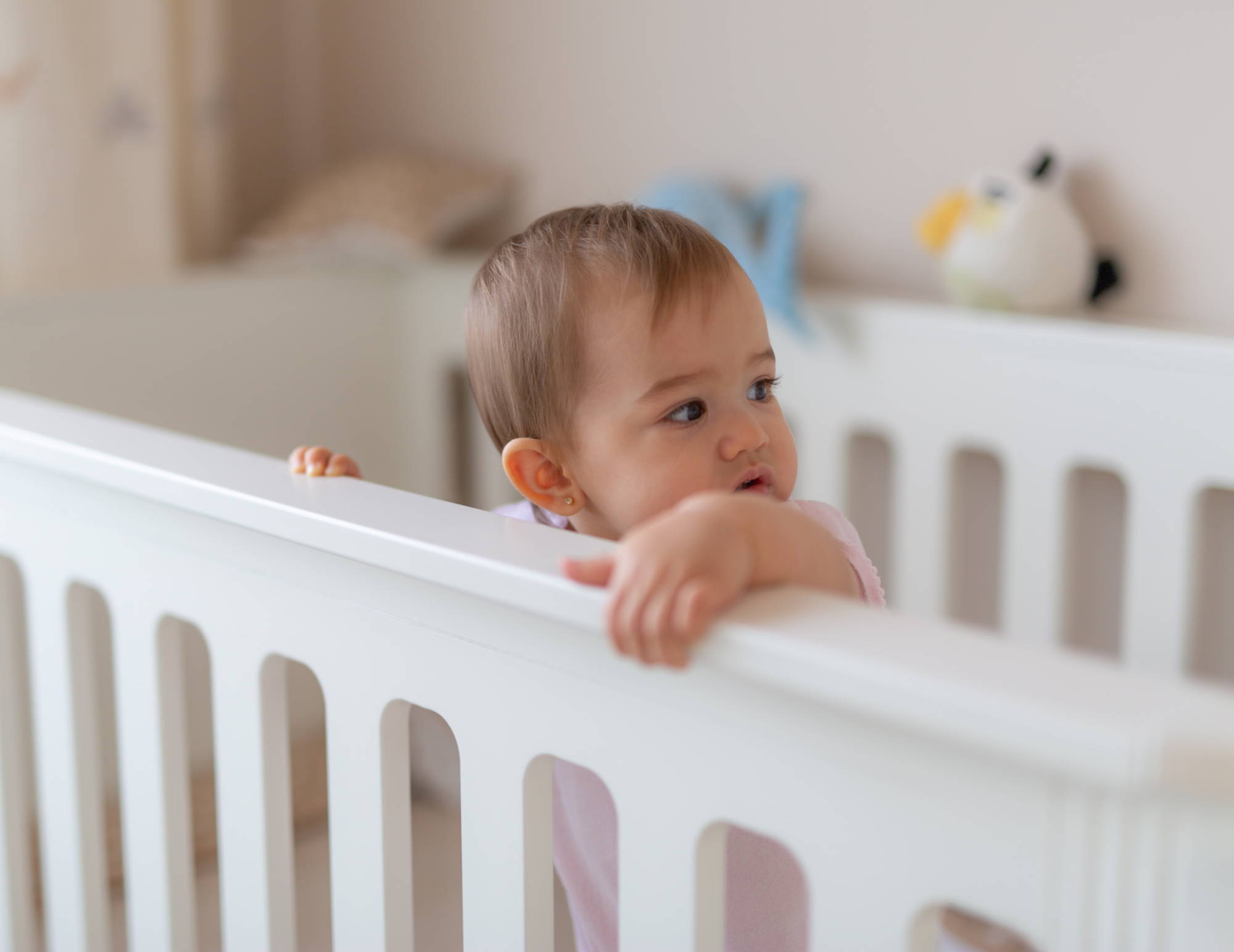 Baby standing up in a white crib in her nursery.