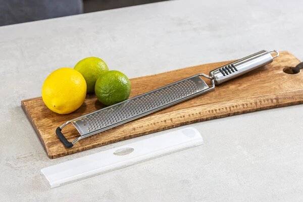 A zester with one lemon and two limes on a wooden board.