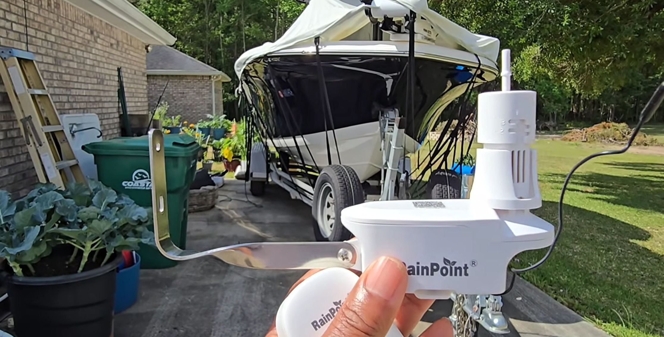 Person holding a device near a parked boat and garden area.