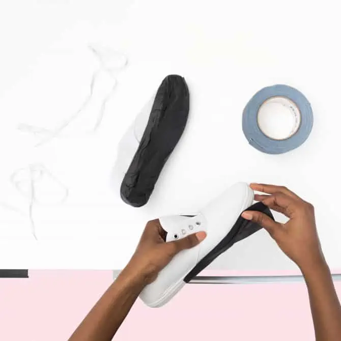 Hands holding a shoe with a roll of tape nearby.