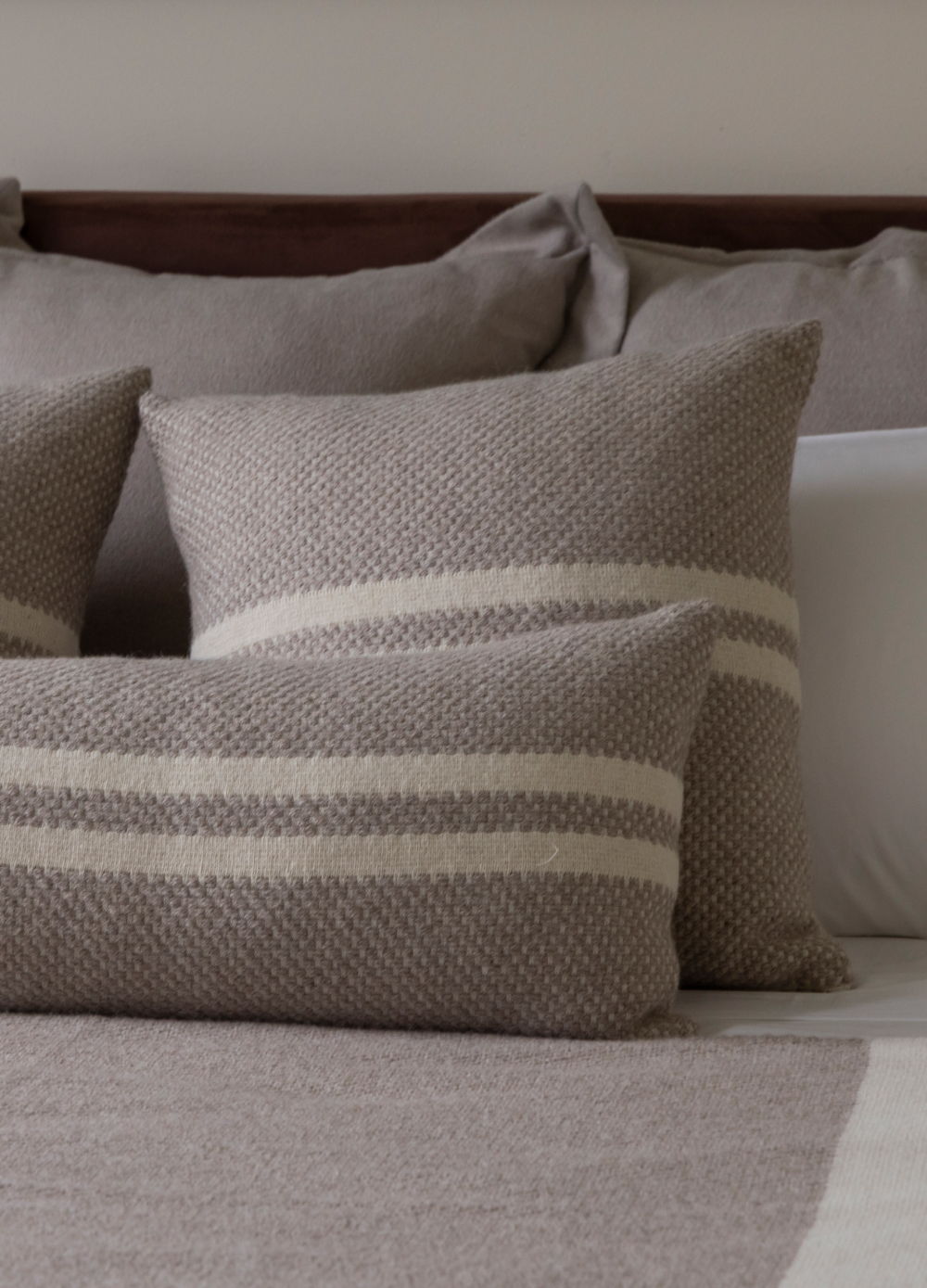 Decorative pillows on a bed with neutral tones and striped patterns.