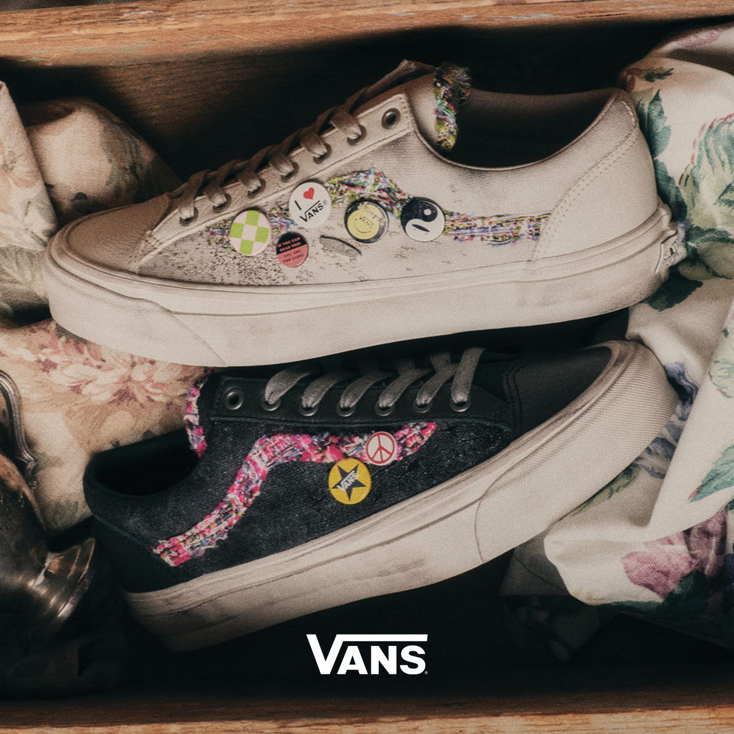Two pairs of Vans shoes with decorative patches, resting in a box.