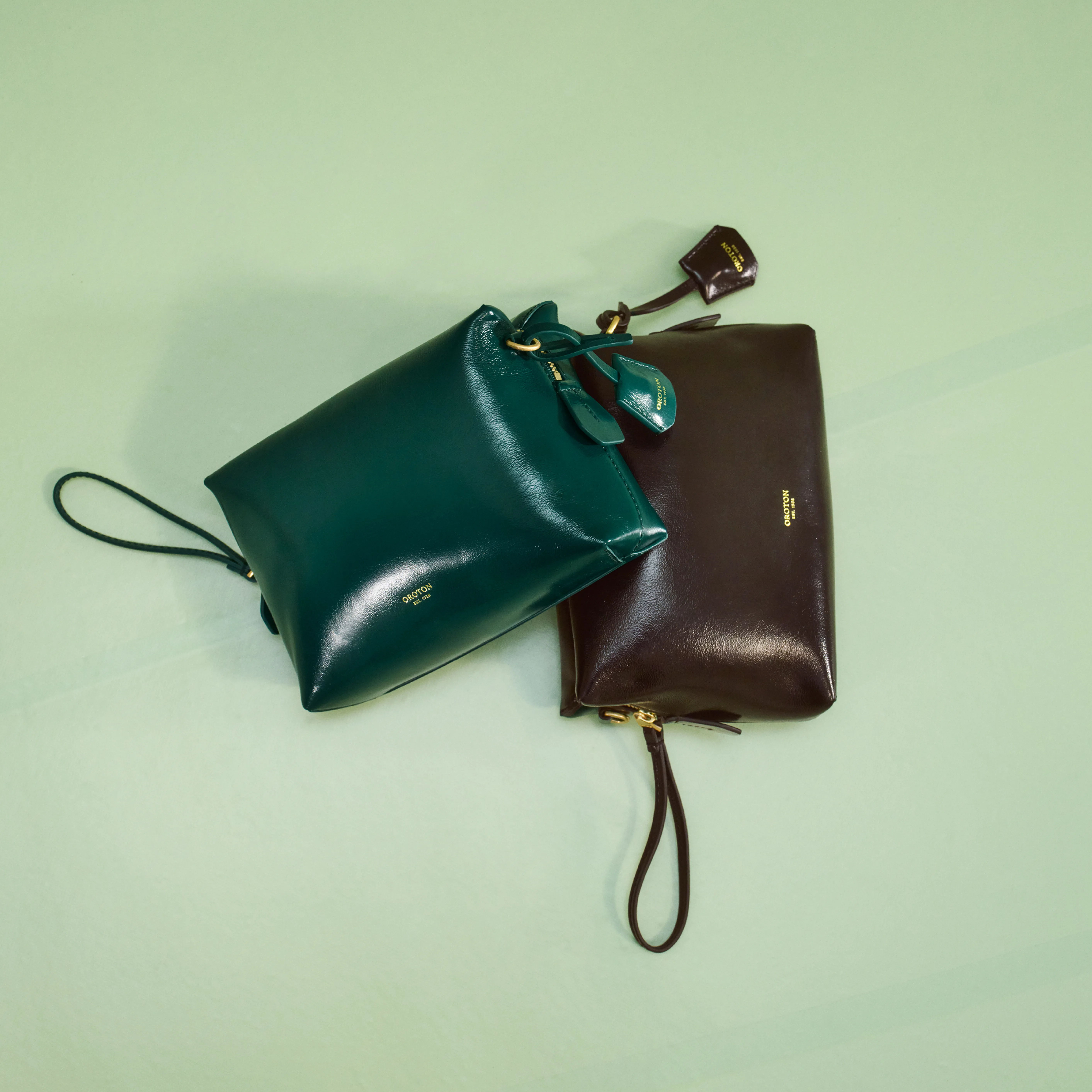 Two leather bags, one green and one brown, on a light green background.