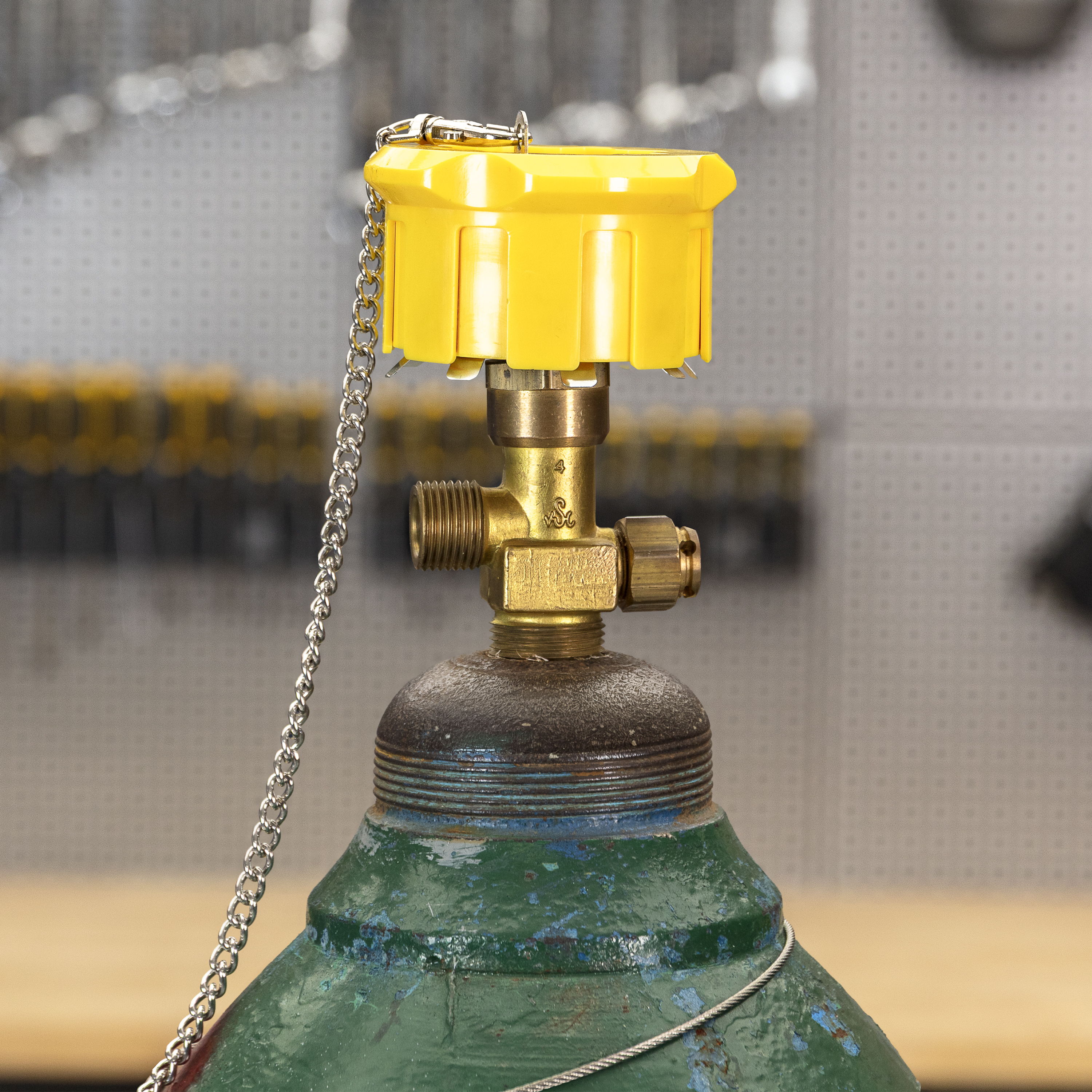 Yellow valve on a green gas cylinder with tools in the background.