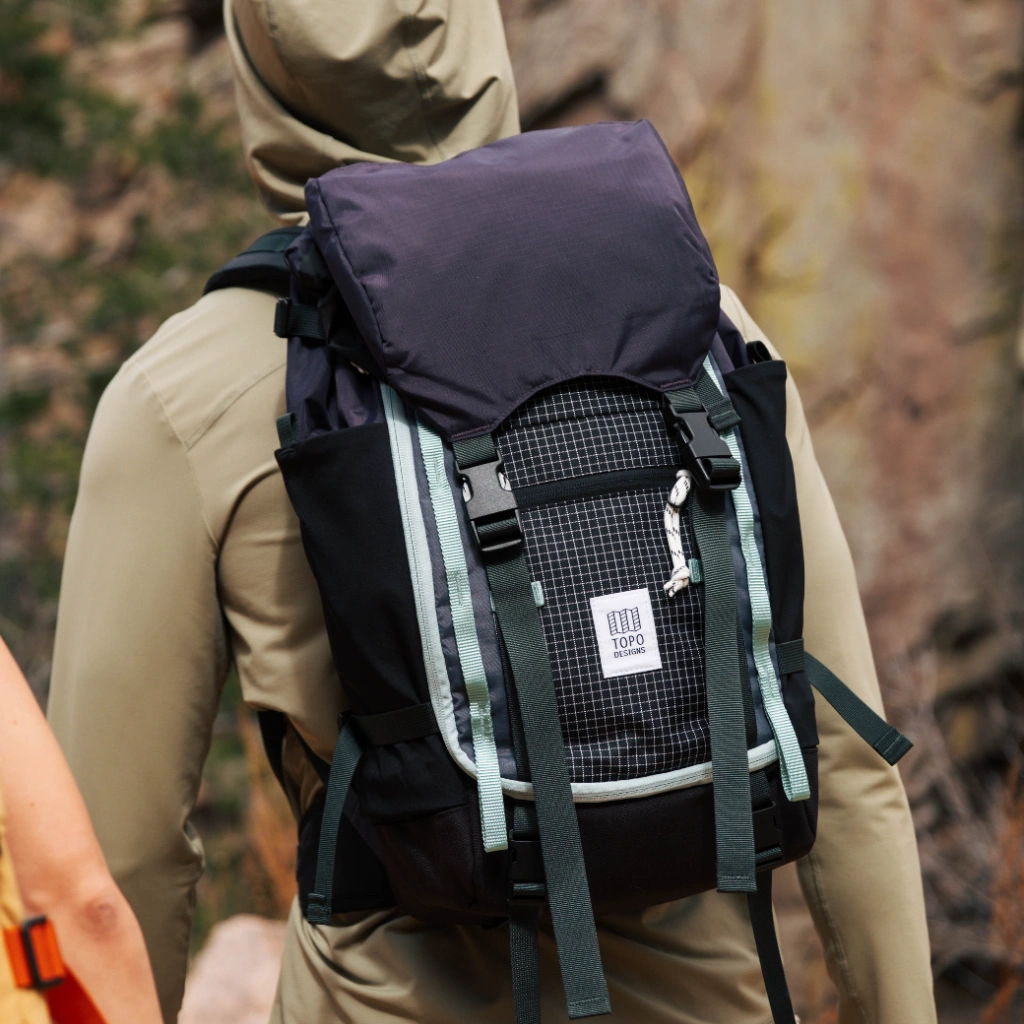 Person wearing a hoodie carrying a black and purple backpack outdoors.