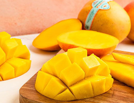 Fresh mango slices on a wooden board with whole mangoes in the background.