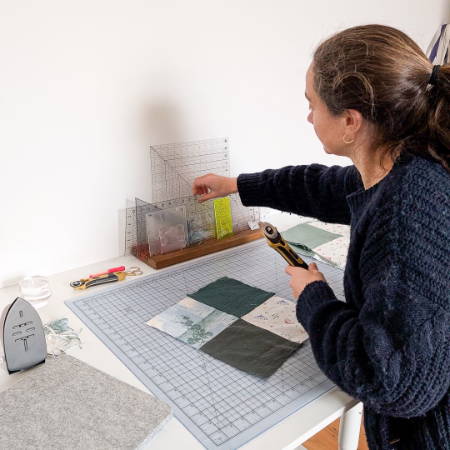 A women grabbing a ruler out of a quilt ruler holder and other sewing tools on a cutting table