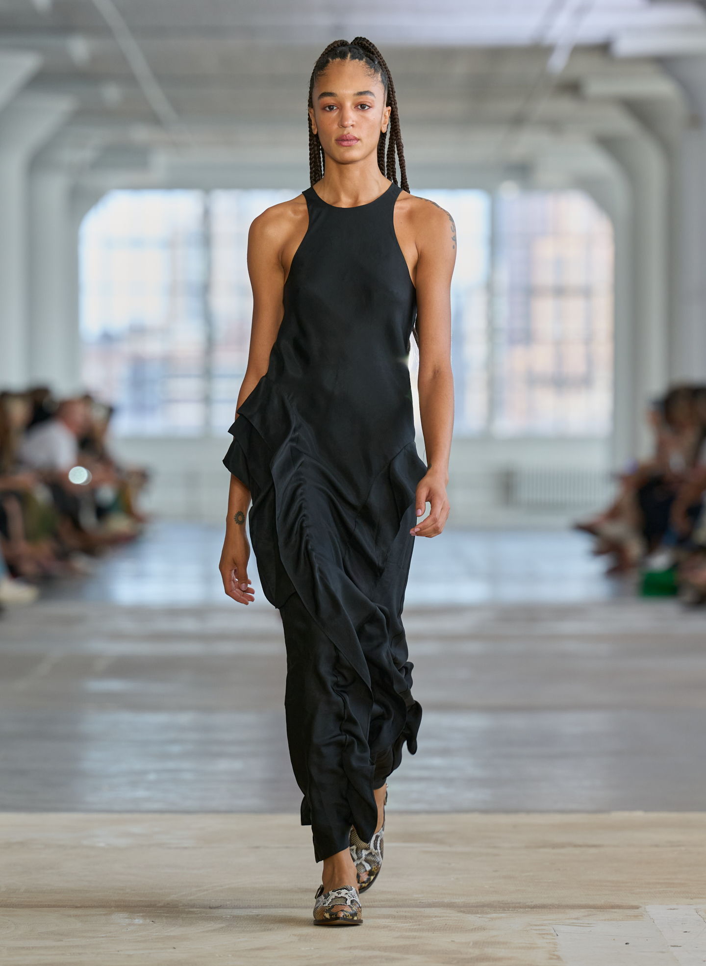 Model walking down runway in a flowing black dress.