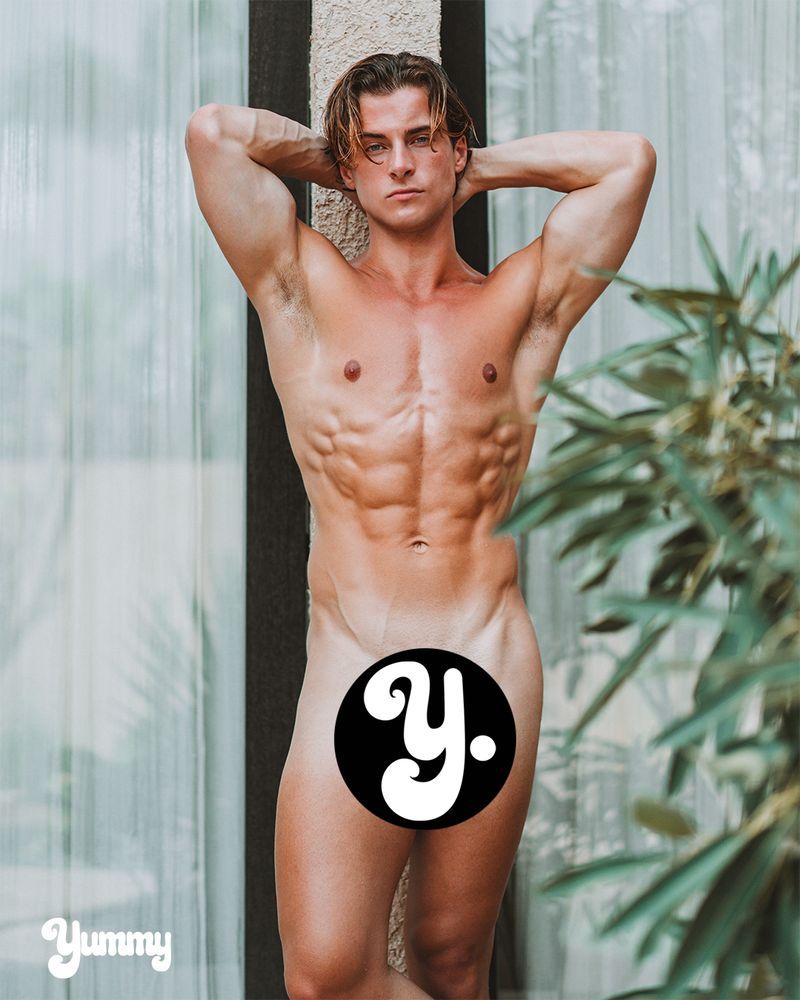 A muscular person posing outdoors with hands behind head, partially obscured by a logo.