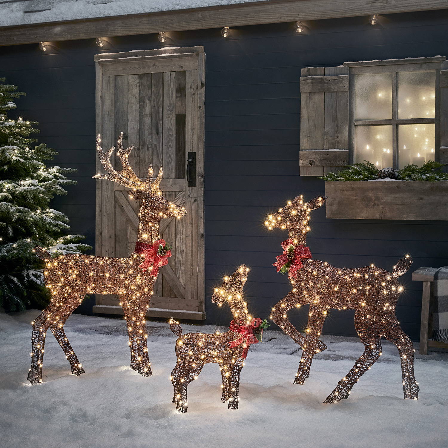 Reindeer family outside in a snowy setting with red bows.