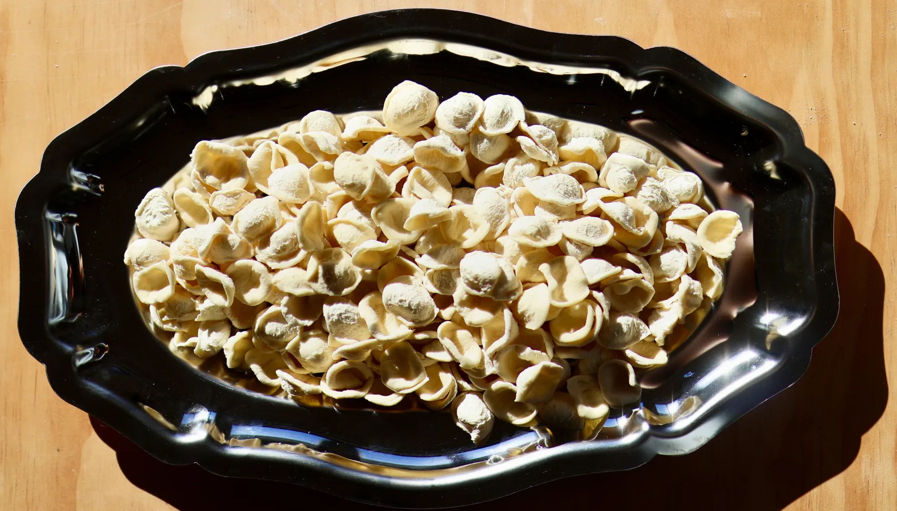 A plate of uncooked pasta shapes on a wooden surface.