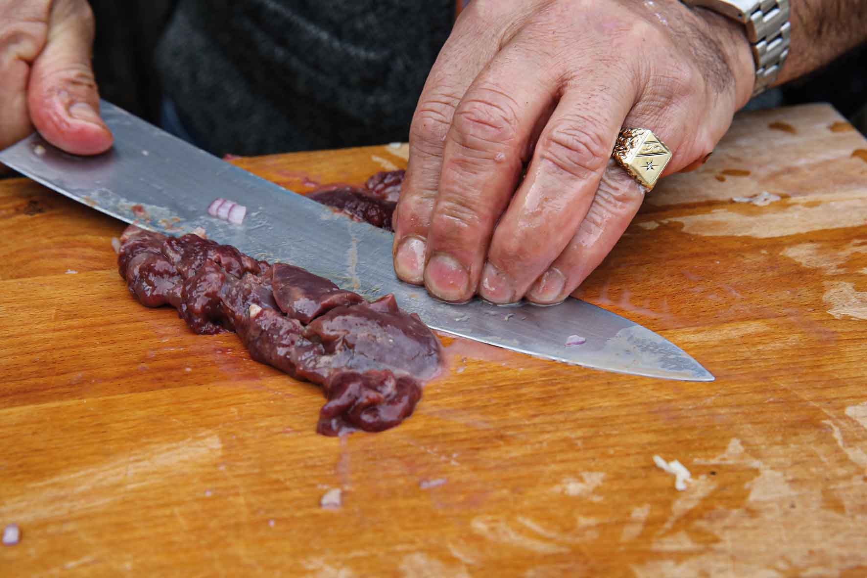 Person slicing meat on a wooden cutting board with a knife.