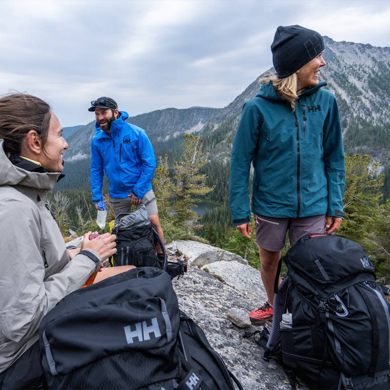 Man & two women wearing Helly Hansen jackets in a mountain setting.