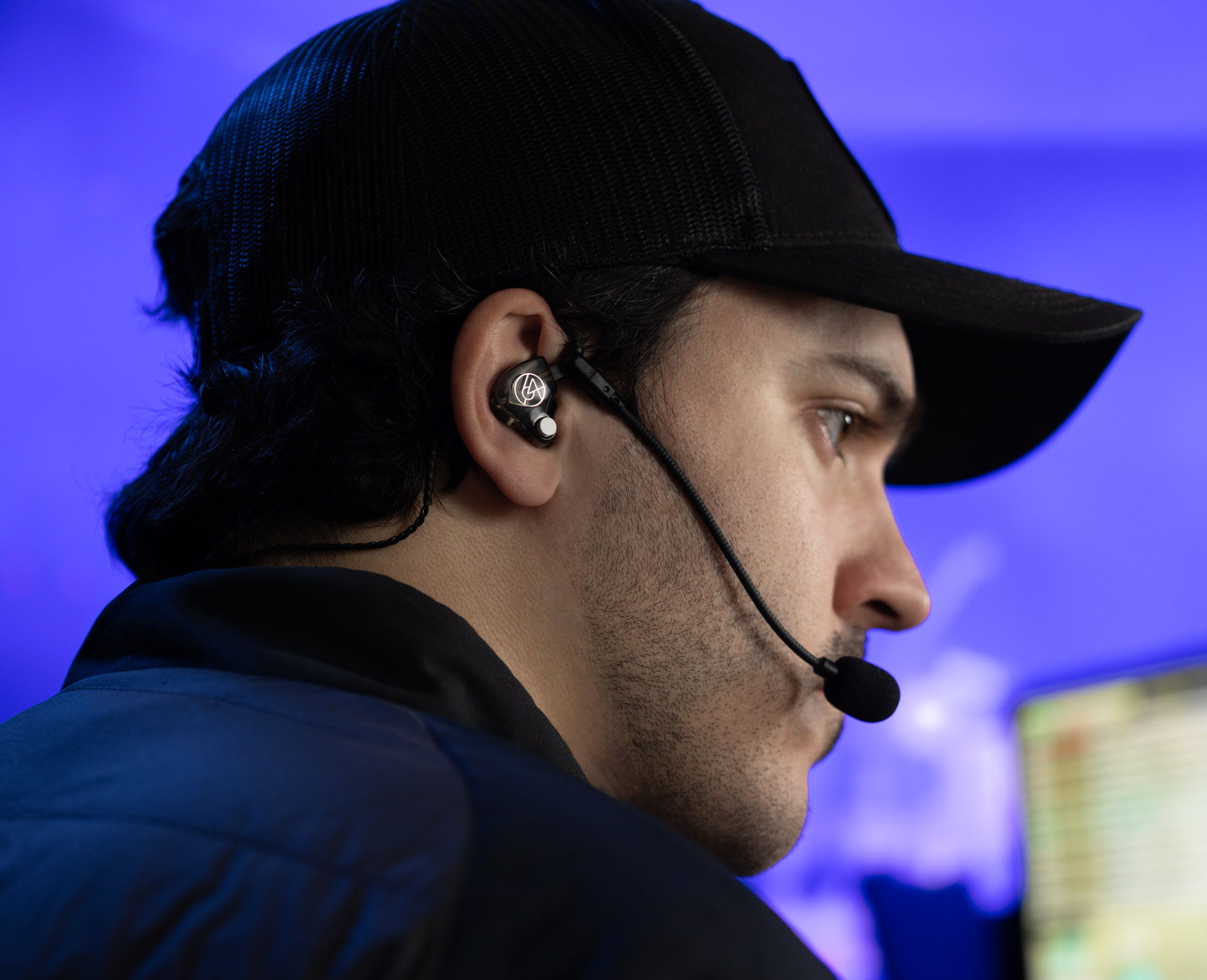Person wearing a headset and cap, focused on a computer screen.