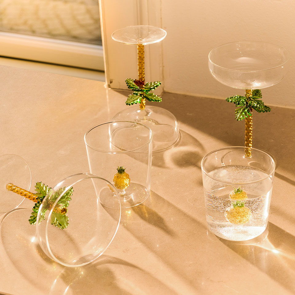 Four decorative glasses with pineapple and leaf designs on a table.