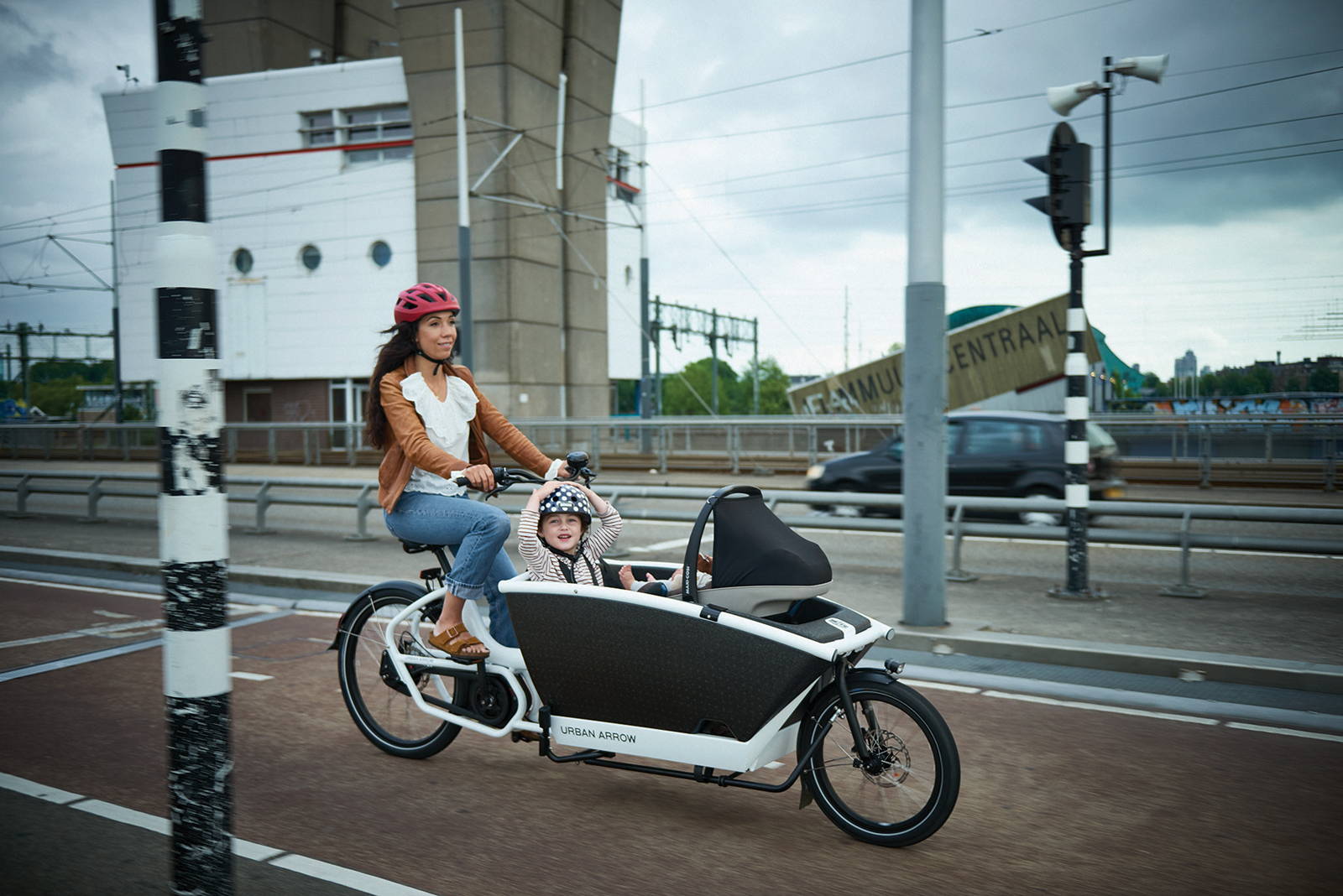 A mum rides her Urban Arrow cargo bike with two young children in the front box across a bridge in Amsterdam.